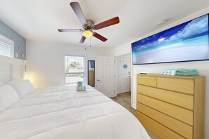 Un dormitorio con una cama grande, un ventilador de techo, un aparador de madera y un televisor de pared que muestra una escena de playa.