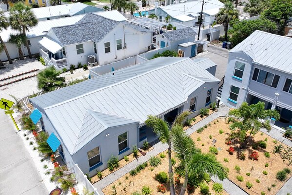 A residential area with multiple houses, each featuring a sloped metal roof and a small front yard with various plants.