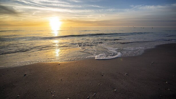 A beach with waves and a sunset.