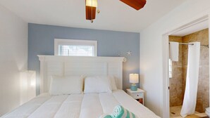 A bedroom with a large bed, a nightstand, a lamp, and a view of a bathroom with a shower.
