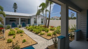 Una casa moderna con un porche cubierto, un sendero y un jardín con diversas plantas y una silla azul.