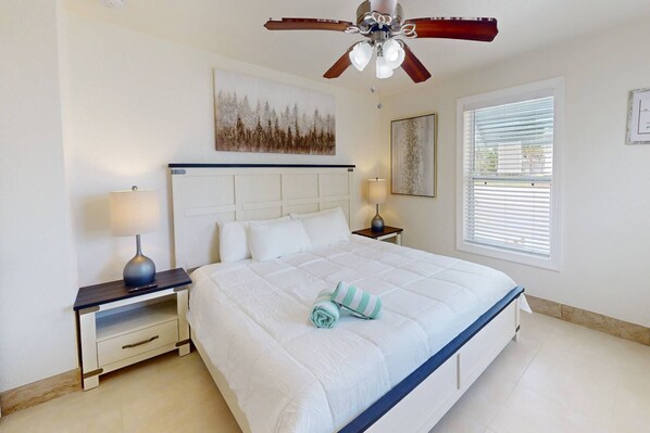 A bedroom with a bed, two bedside tables, a ceiling fan, and a window with blinds.