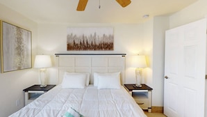 Una habitación de hotel con una cama grande, dos mesitas de noche, un ventilador de techo y una puerta.