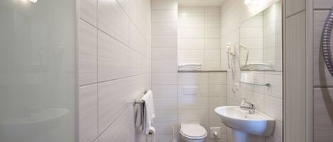 Een moderne badkamer met witte tegels, een toilet, een wastafel en een douchecabine van glas.