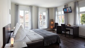 Ein modernes Hotelzimmer mit Bett, Nachttisch, Schreibtisch und Fernseher.