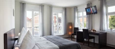 A modern hotel room with a bed, bedside table, desk, and TV.