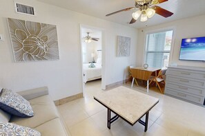 A spacious living area with a sofa, a coffee table, a dining table with chairs, a ceiling fan, and artwork on the walls.