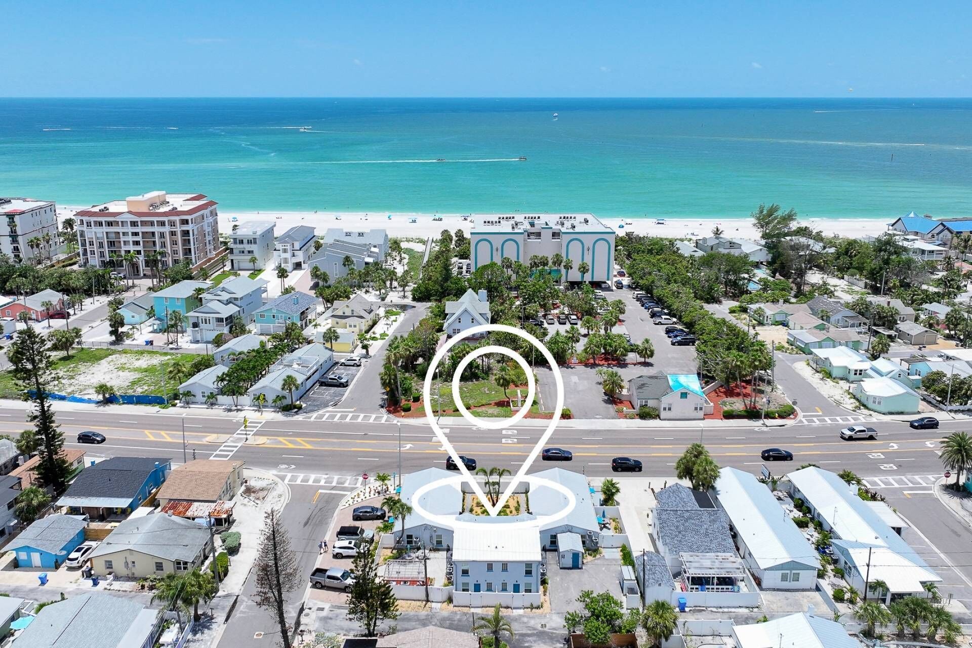 A coastal town with a beachfront hotel, a parking lot, and a clear view of the ocean.