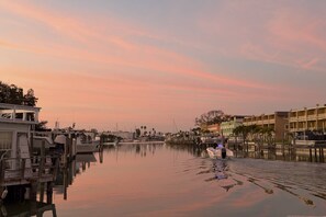 A waterfront marina with boats docked, a calm water surface, and buildings in the background.