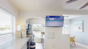 Una cocina moderna con un televisor grande, un cubo de basura y una zona de comedor con una mesa y sillas.
