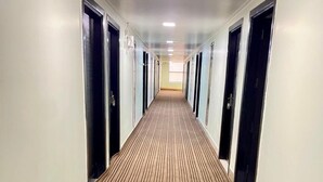 A long, narrow hallway with a patterned carpet, white walls, and doors on both sides. - Sumedha Elegance (Gurugram)