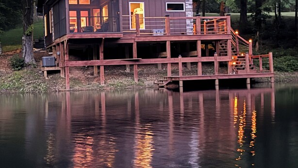 Eine Holzhütte mit Balkon und Steg, der über einen ruhigen See führt, umgeben von Bäumen.