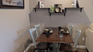 A dining room with a wooden table, white chairs, and shelves above holding books and decorative items.
