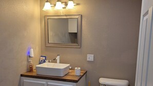 A bathroom with a white sink, mirror, and toilet. There are three wall-mounted lights above the mirror.
