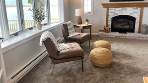 A living room with two leather chairs, a fireplace, a TV, and a view of a lake. - 3BR Sandy Pond LAKE HOUSE | Dock | Fire Pit | Pets (Pulaski)