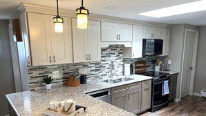 A modern kitchen with granite countertops, white cabinets, a black stove, and a tiled backsplash. - 3BR Sandy Pond LAKE HOUSE | Dock | Fire Pit | Pets (Pulaski)
