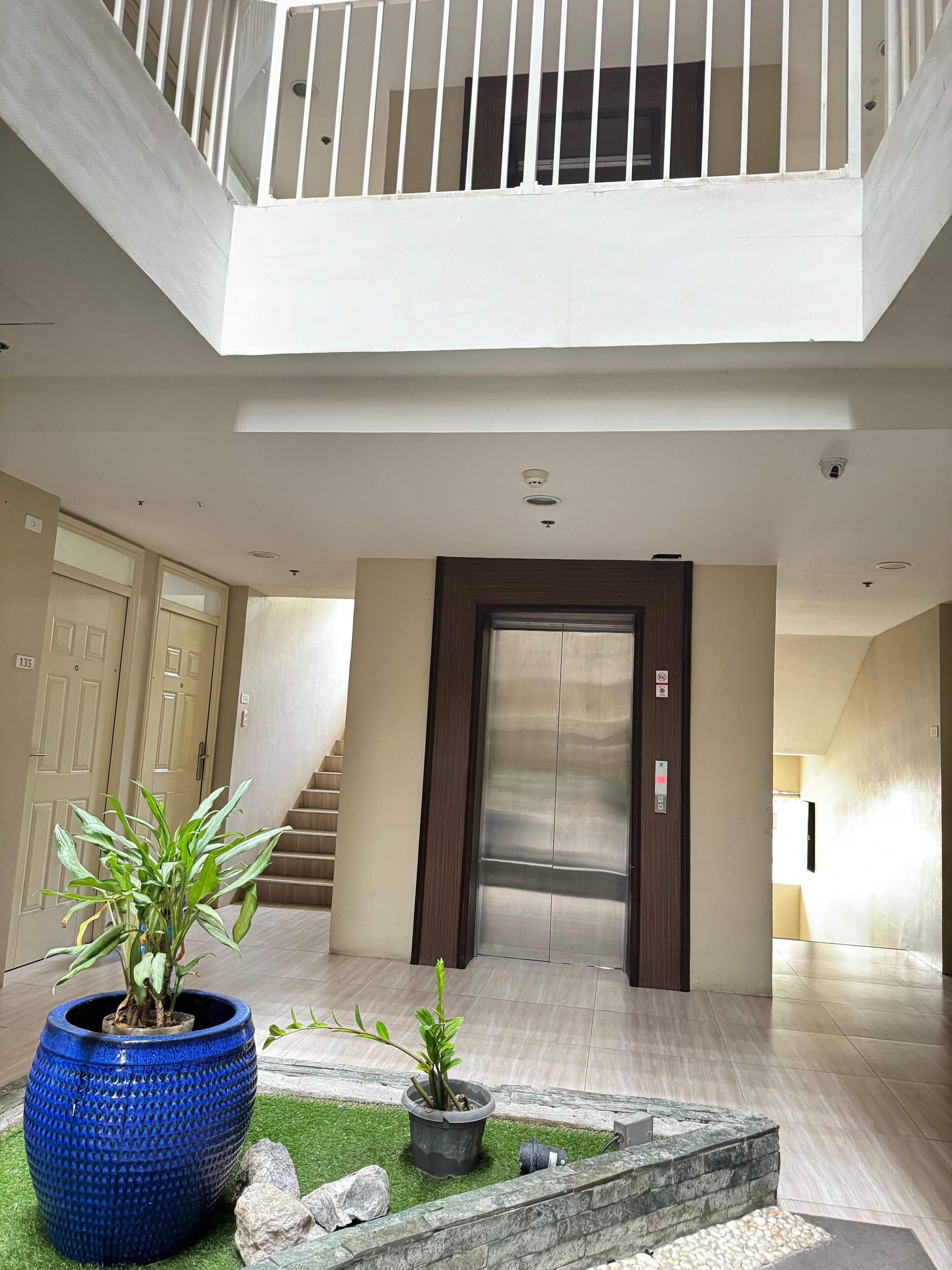 Un vaste espace intérieur comprenant un escalier, un grand pot bleu contenant une plante, et un petit jardin agrémenté de rochers et d’une fontaine.
