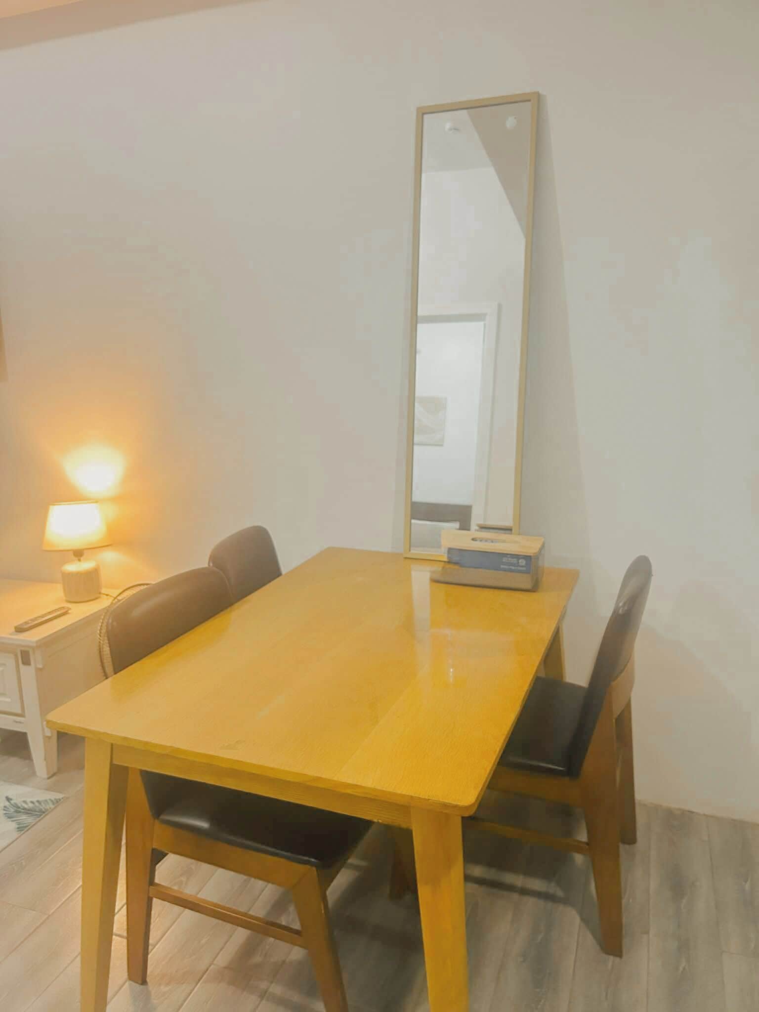 Zona pranzo con tavolo in legno, quattro sedie, una lampada e uno specchio appeso al muro.