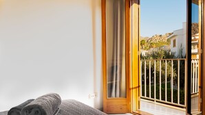 Un dormitorio con una cama, una toalla enrollada y un ventanal corredero que da a un balcón con barandilla.