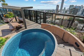 A rooftop pool with a city view, outdoor seating, and a pergola.