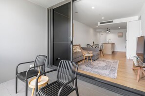 Uma sala de estar moderna com um sofá, duas poltronas, uma mesa pequena e um aparador de vidro.