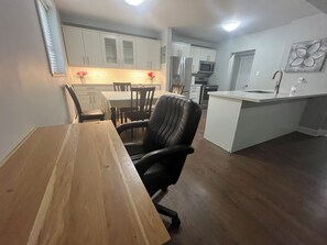 A modern kitchen with white cabinets, a stainless steel refrigerator, and a microwave. There is a dining area with a wooden table and chairs. - Charming 2-bedroom apartment in terrific Burlington with WiFi and free parking (Burlington)