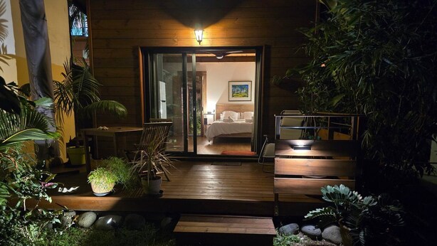 A wooden cabin with a glass door leading to a bedroom, surrounded by potted plants and a wooden deck.