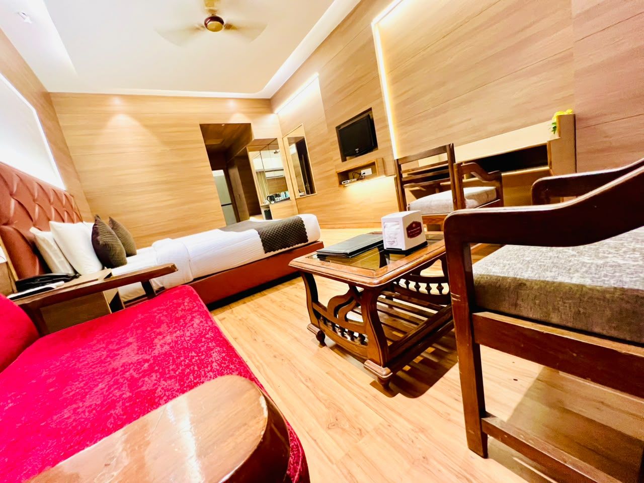 A hotel room with a wooden floor, a red sofa, a wooden coffee table, and a bed with a headboard.