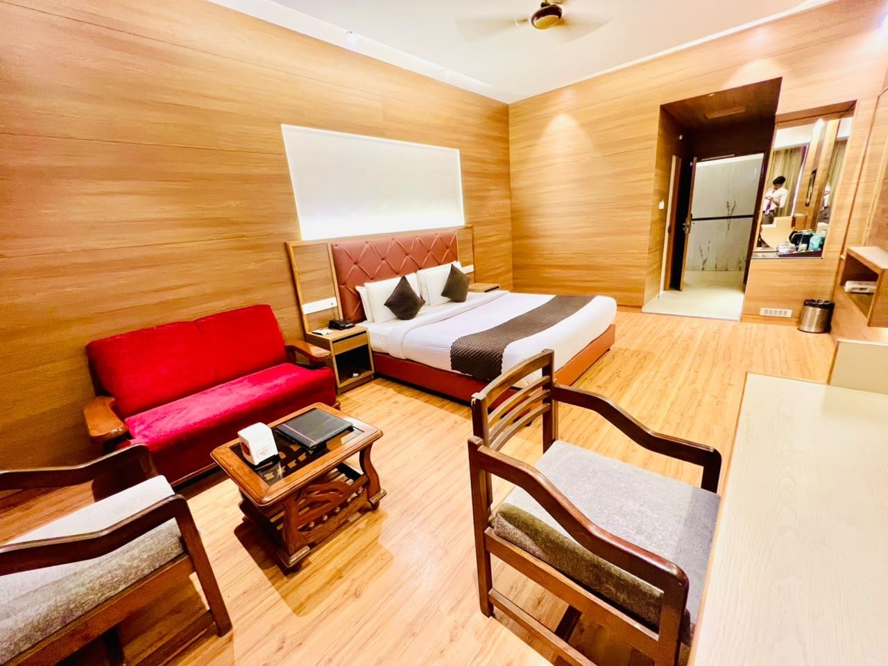 Een hotelkamer met een bed, een rode bank, een houten salontafel en een stoel.