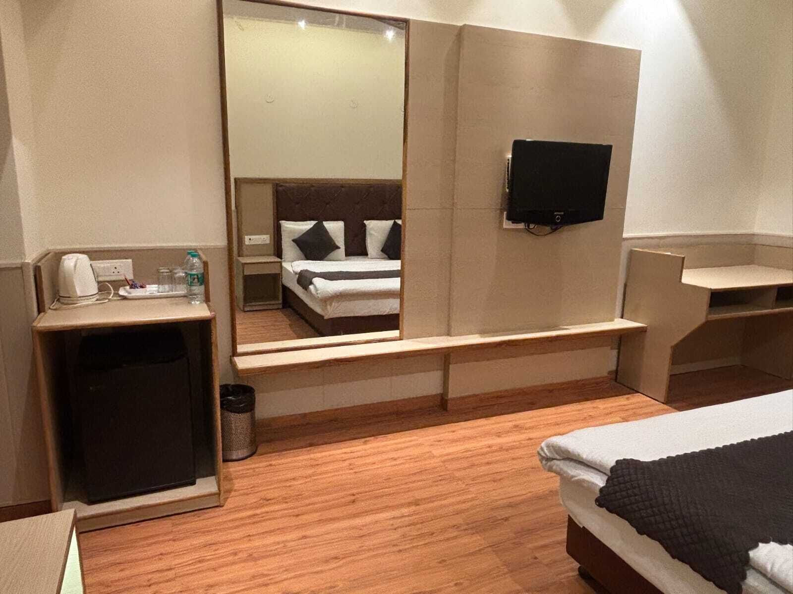 A hotel room with a bed, a desk, a mirror, a television, and a trash can.