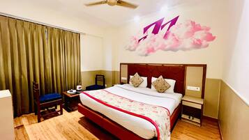 A hotel room with a large bed, a ceiling fan, a desk with a chair, and a wall with a cloud mural.