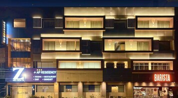 Un hotel a più piani con una facciata moderna, caratterizzato da balconi e insegne illuminate per AP Residency e Barista.