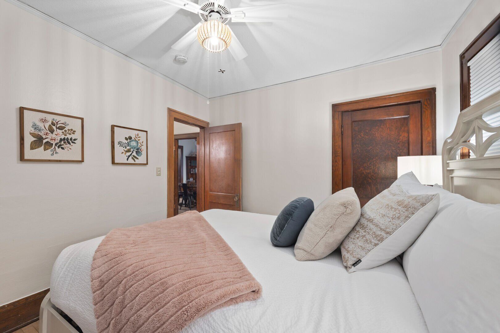 A bedroom with a bed, a ceiling fan, and two framed floral artworks on the wall.