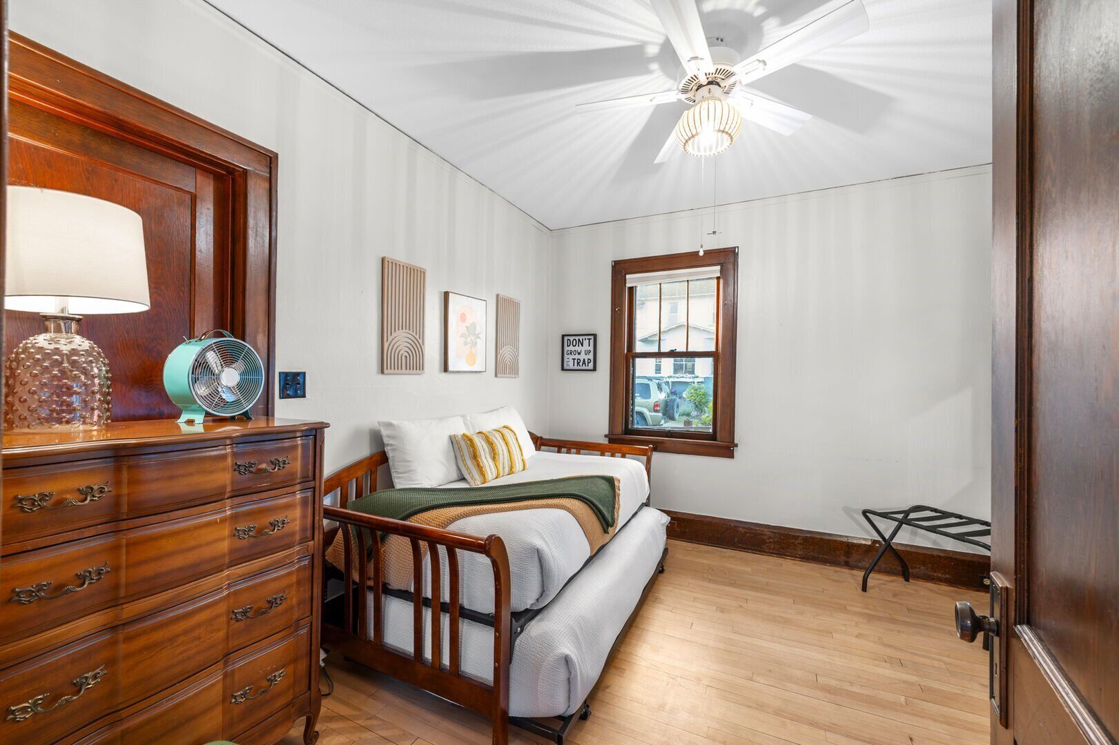 A bedroom with a wooden dresser, a bed with a green blanket, and a ceiling fan.