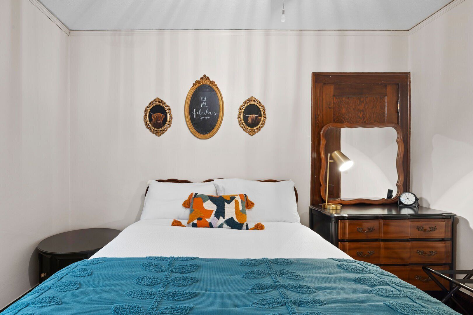 A bedroom with a bed, a dresser, a mirror, and three framed pictures on the wall.