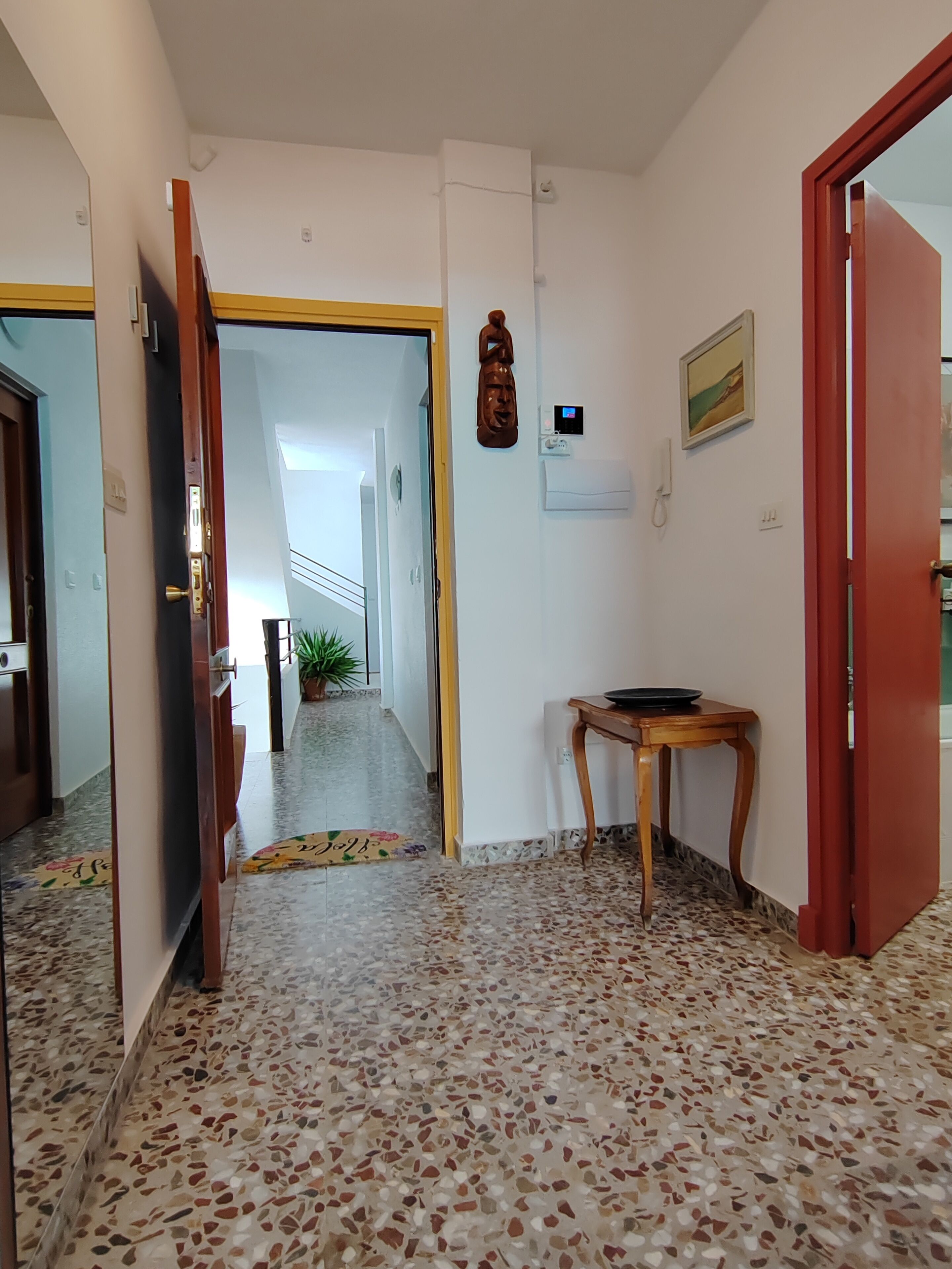 Un couloir doté d’un sol en terrazzo, d’une table en bois, d’un climatiseur fixé au mur et d’une porte donnant sur une autre pièce.
