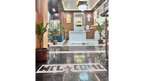 Un hall d’accueil d’hôtel avec un tapis où est écrit « BIENVENUE », un comptoir de réception et des plantes en pot.