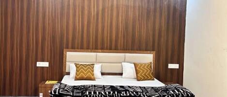 Un dormitorio con pared de paneles de madera, una cama con ropa de cama estampada, una mesita de noche y un ventilador de techo.
