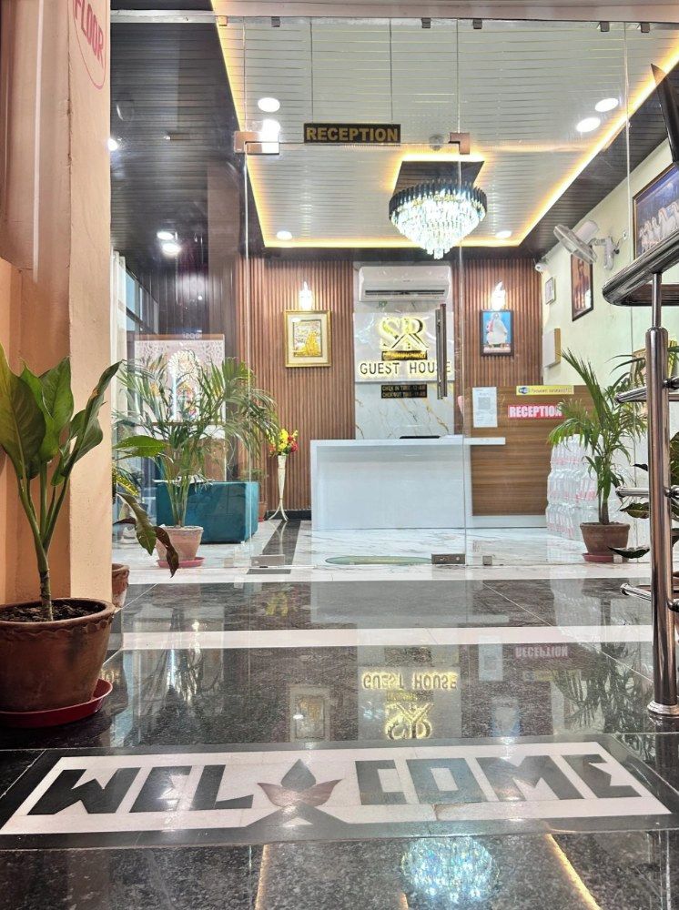 A hotel reception area with a 'WELCOME' mat, reception desk, and potted plants.