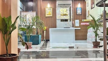 A hotel reception area with a 'WELCOME' mat, reception desk, and potted plants.