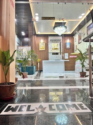 A hotel reception area with a 'WELCOME' mat, reception desk, and potted plants. - S R GUEST HOUSE (Umaraha)