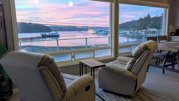Ein Zimmer mit zwei Liegesesseln, die auf ein großes Fenster mit Blick auf einen See und Boote zeigen.