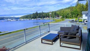 Ein Balkon mit einer Couch und einem Tisch, mit Blick auf einen Yachthafen mit Booten und eine bewaldete Hügelslandschaft.