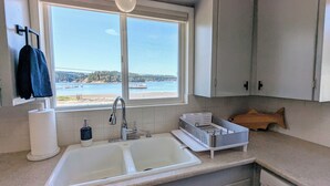 Eine Küche mit einem doppelten Spülbecken, einem Fenster mit Blick auf den Strand und einer Holz-Fischdekoration auf der Arbeitsplatte.