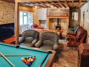 A cozy room with a pool table, leather chairs, a fireplace, and stone walls.