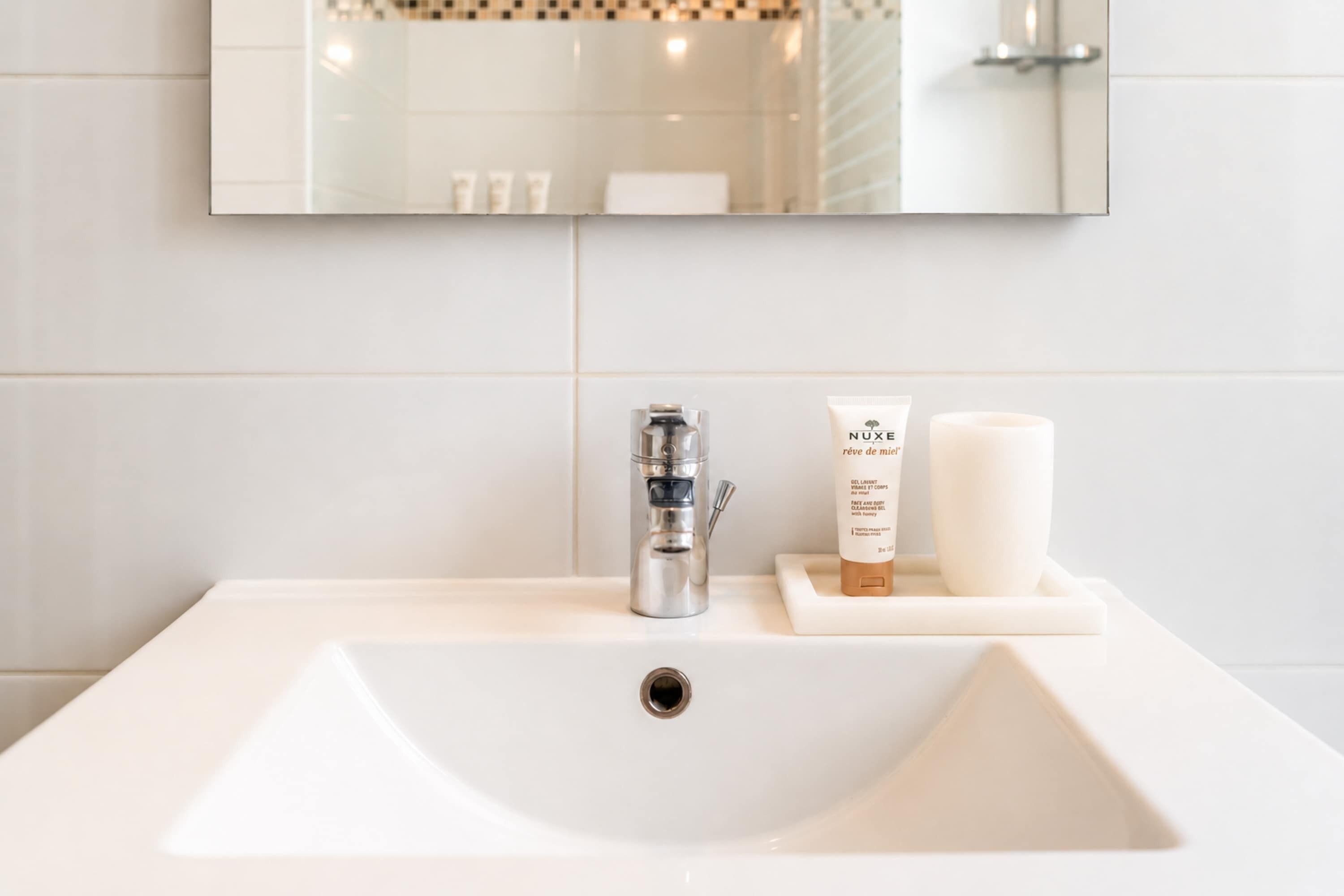 A bathroom sink with a mirror above it, a faucet, and two toiletry items on the sink's edge.