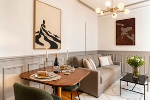 A dining area with a table set for two, a sofa, and a decorative vase with flowers.