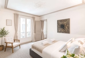 A bedroom with a bed, a chair, a potted plant, and a door leading to an outdoor balcony.