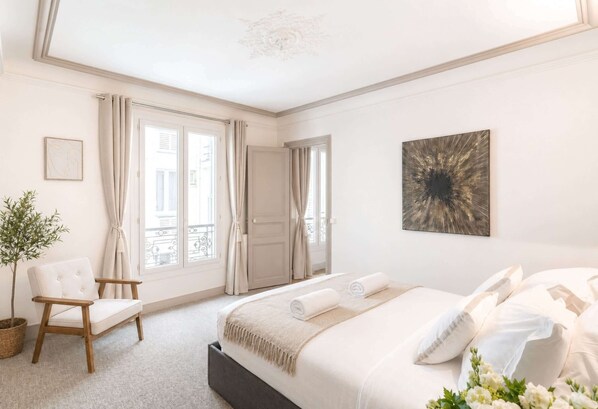 Un dormitorio con cama, una silla, una planta en maceta y una puerta que da a un balcón exterior.