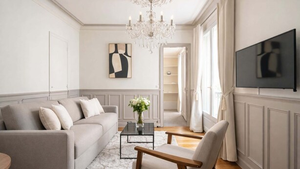 A living room with a sofa, armchair, coffee table, TV, chandelier, and artwork. - Trocadero - Elegant apartment with lift (Unknown)